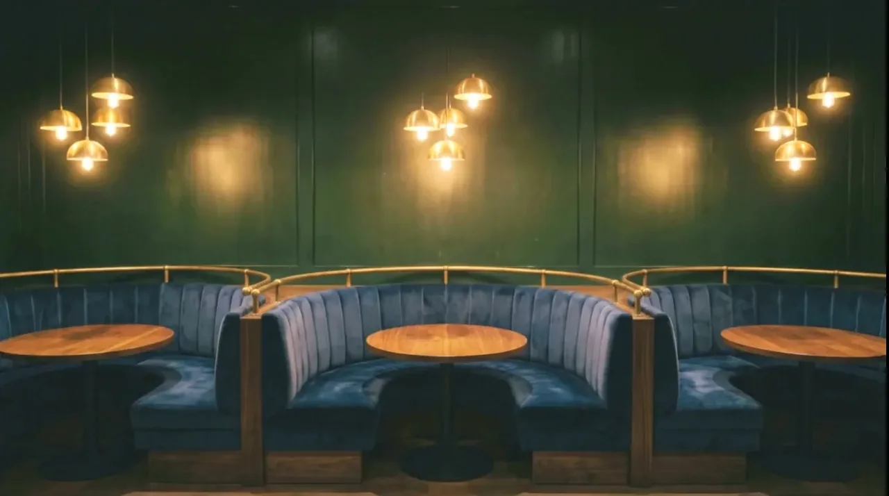 Curved teal velvet booths with round oak tops under brass pendants
