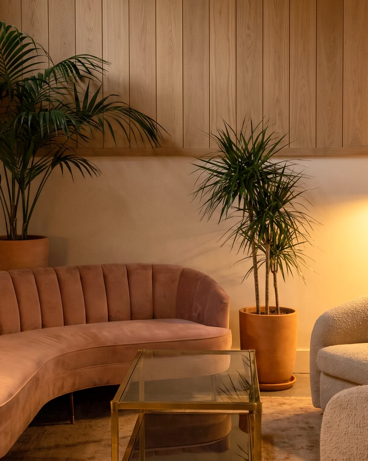Un sofá de terciopelo rosa empolvado con respaldo acanalado y sillones de bouclé en el lobby de un hotel con paneles de roble