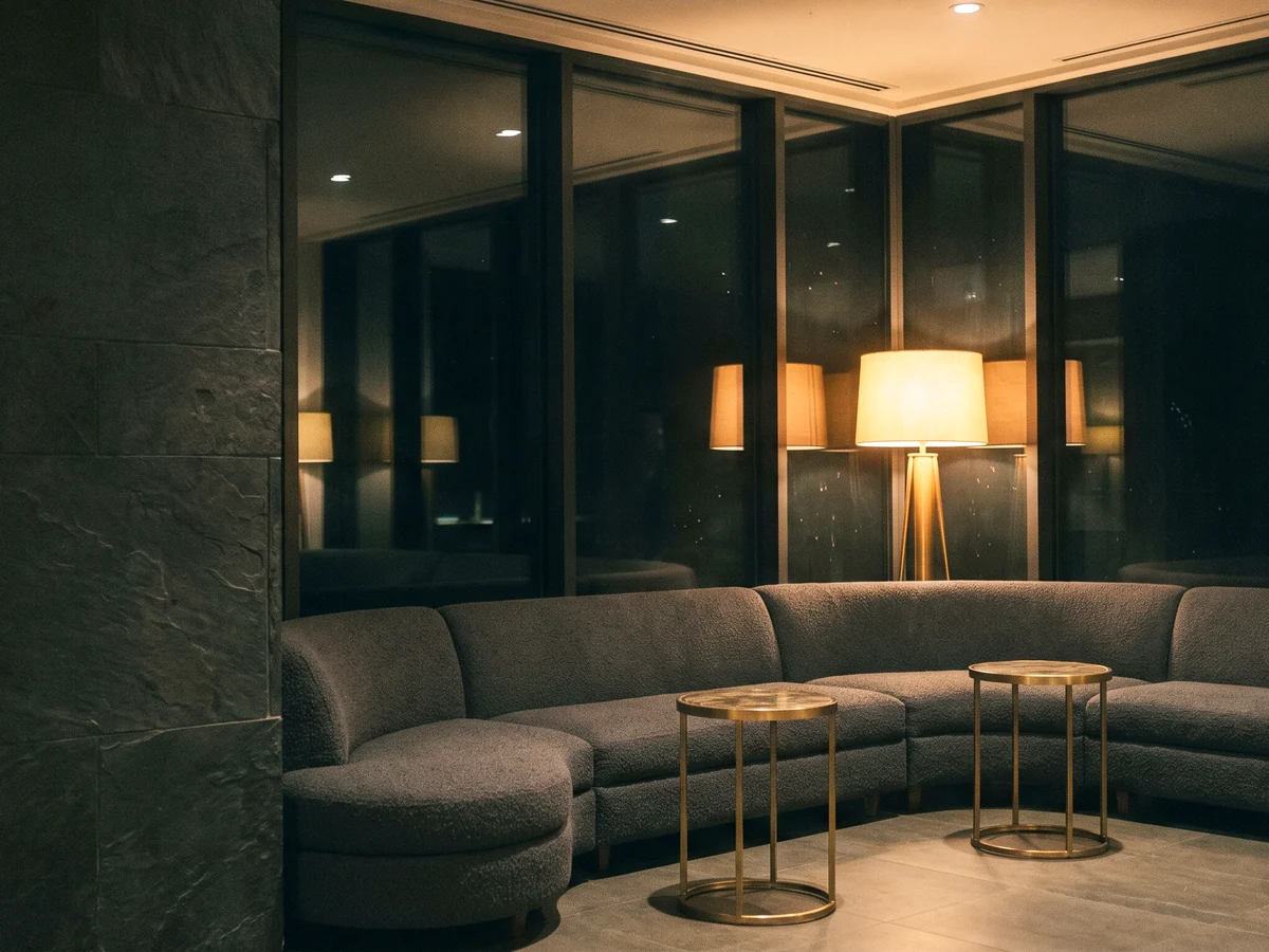 A curved charcoal boucle sectional with brass tables in a hotel lounge at night