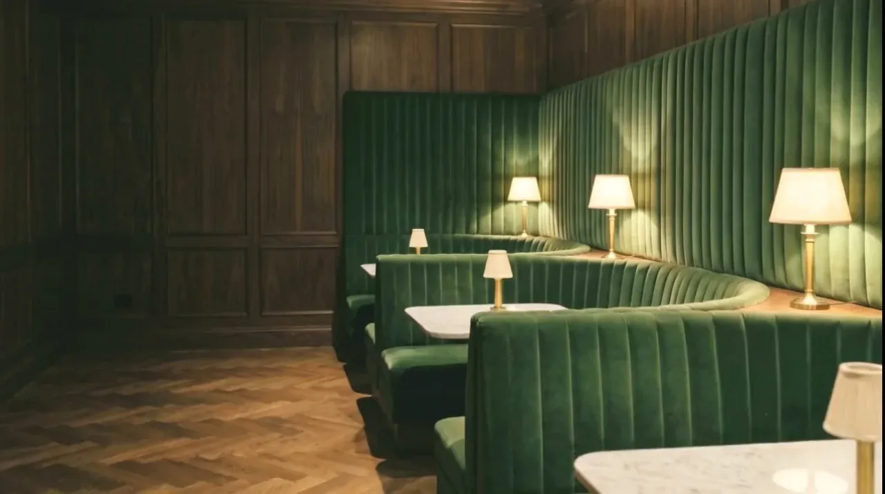 A run of green velvet channel-back banquettes under warm table lamps in a panelled dining room