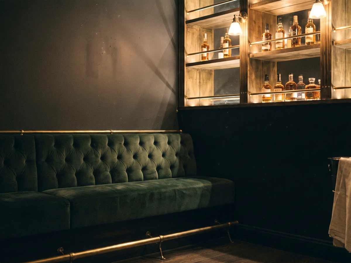 A green velvet diamond-tufted banquette below lit liquor shelving
