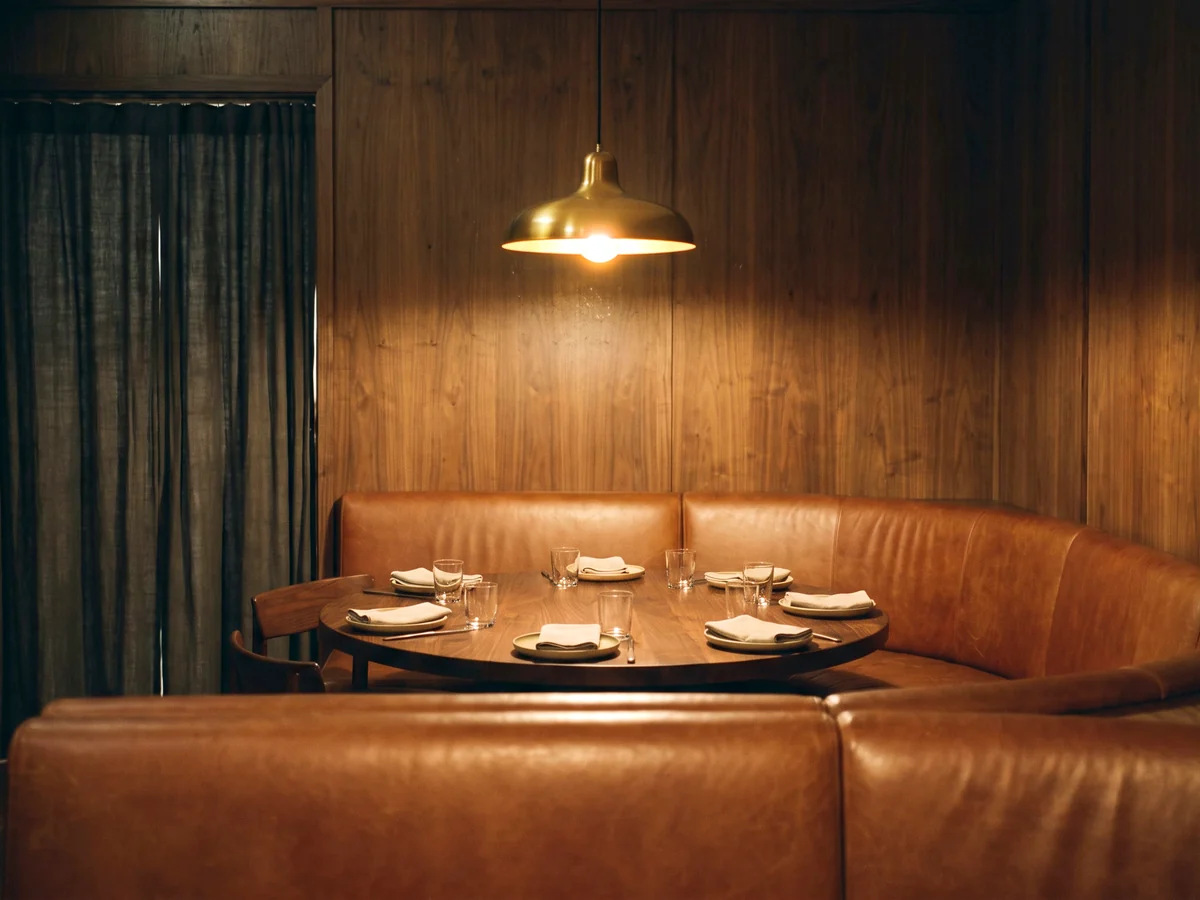 A U-shaped cognac leather booth around a round walnut table in a private dining room