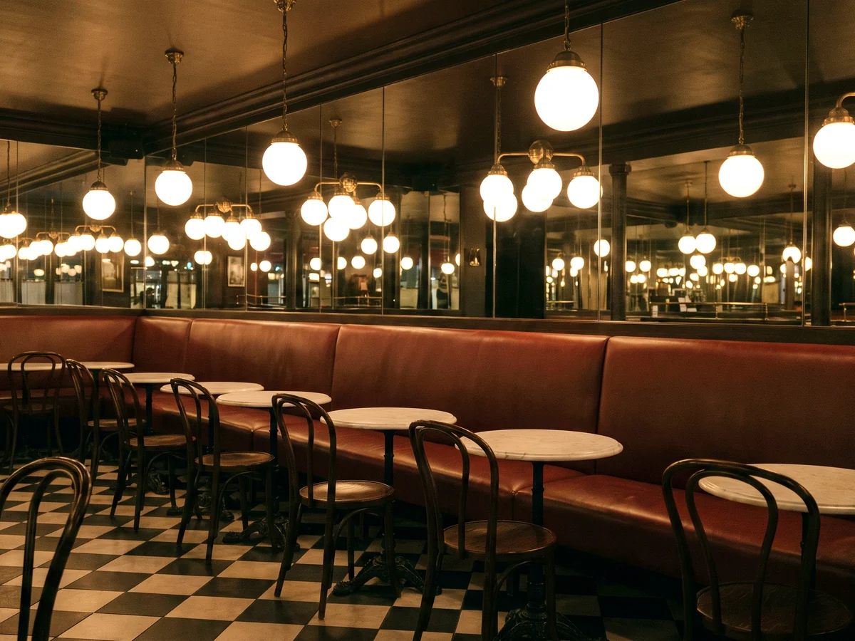 An oxblood leather banquette along a mirrored wall in a brasserie with globe pendants